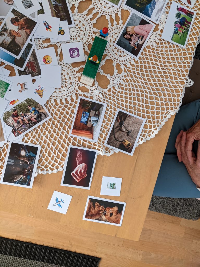 Foto van een tafel van bovenaf. Op de tafel liggen een aantal foto's en afbeeldingen. Ook staat er een bruggetje op van Lego, maar daarop twee poppetjes.